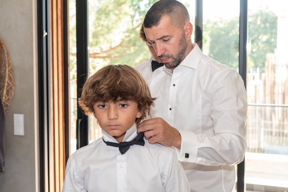 Adult adjusting young boy's bow tie during formal dressing.