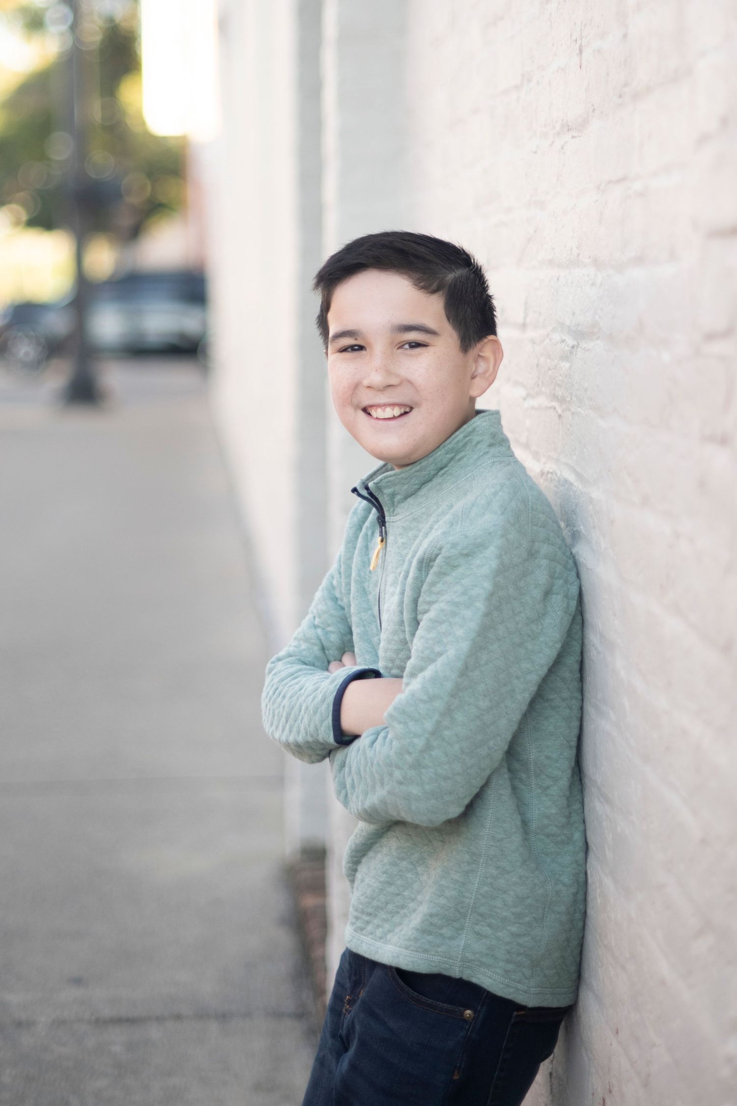Young child in mint green sweater poses playfully against white wall in downtown Franklin