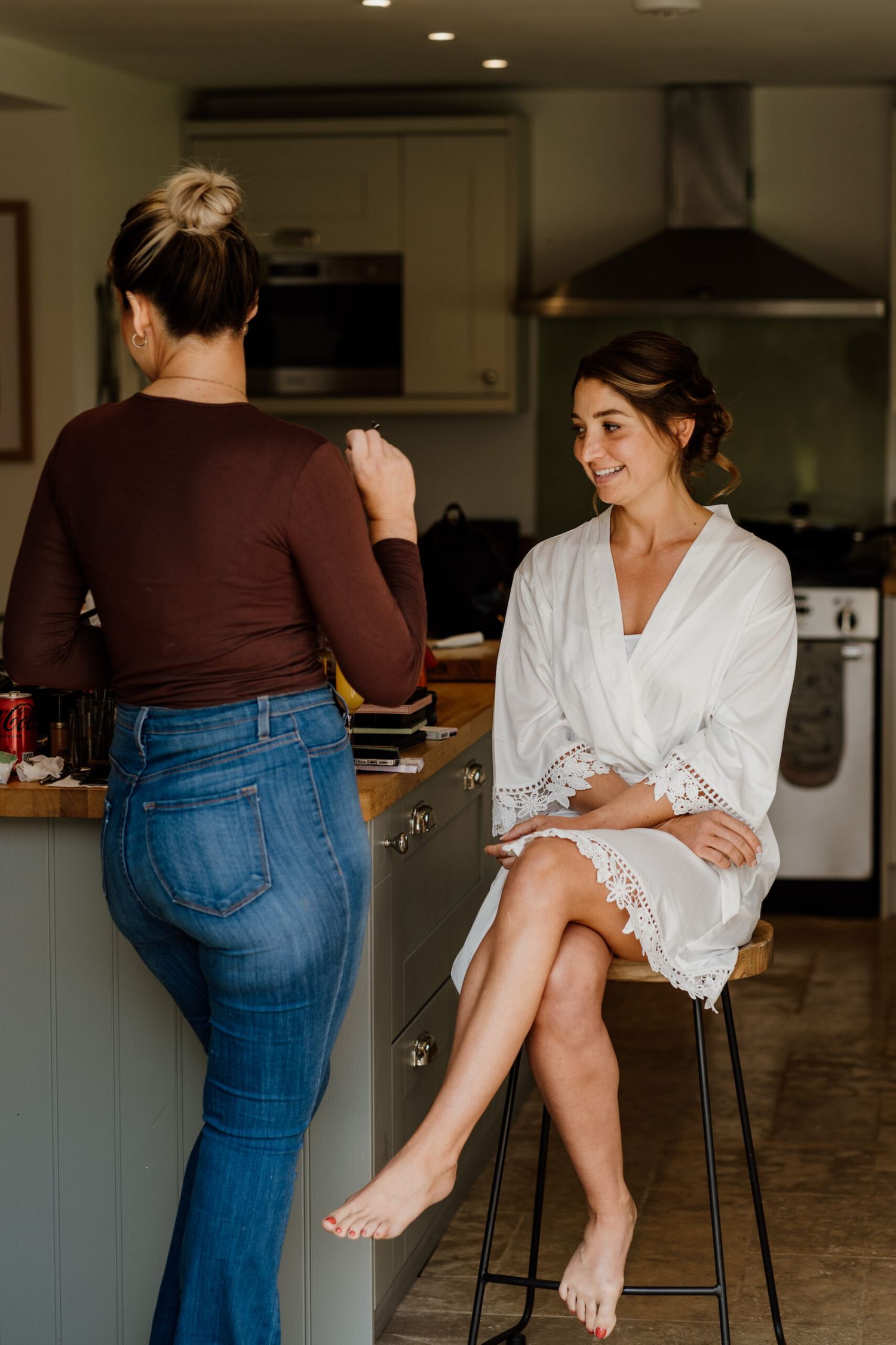 Wedding party members lounging casually in a modern kitchen wearing white robes and jeans.