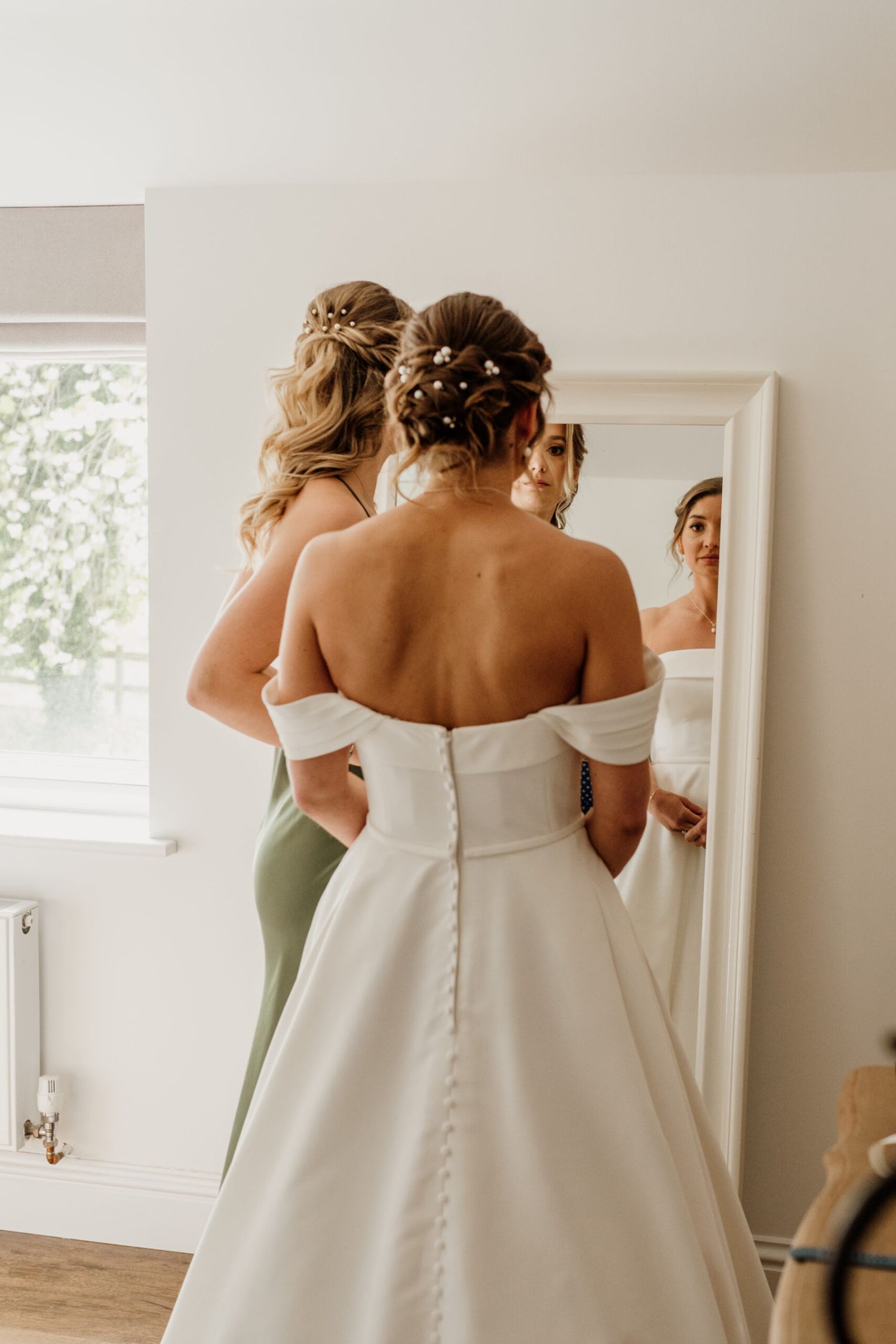 Back details of an elegant off-shoulder wedding dress being fitted with buttons.