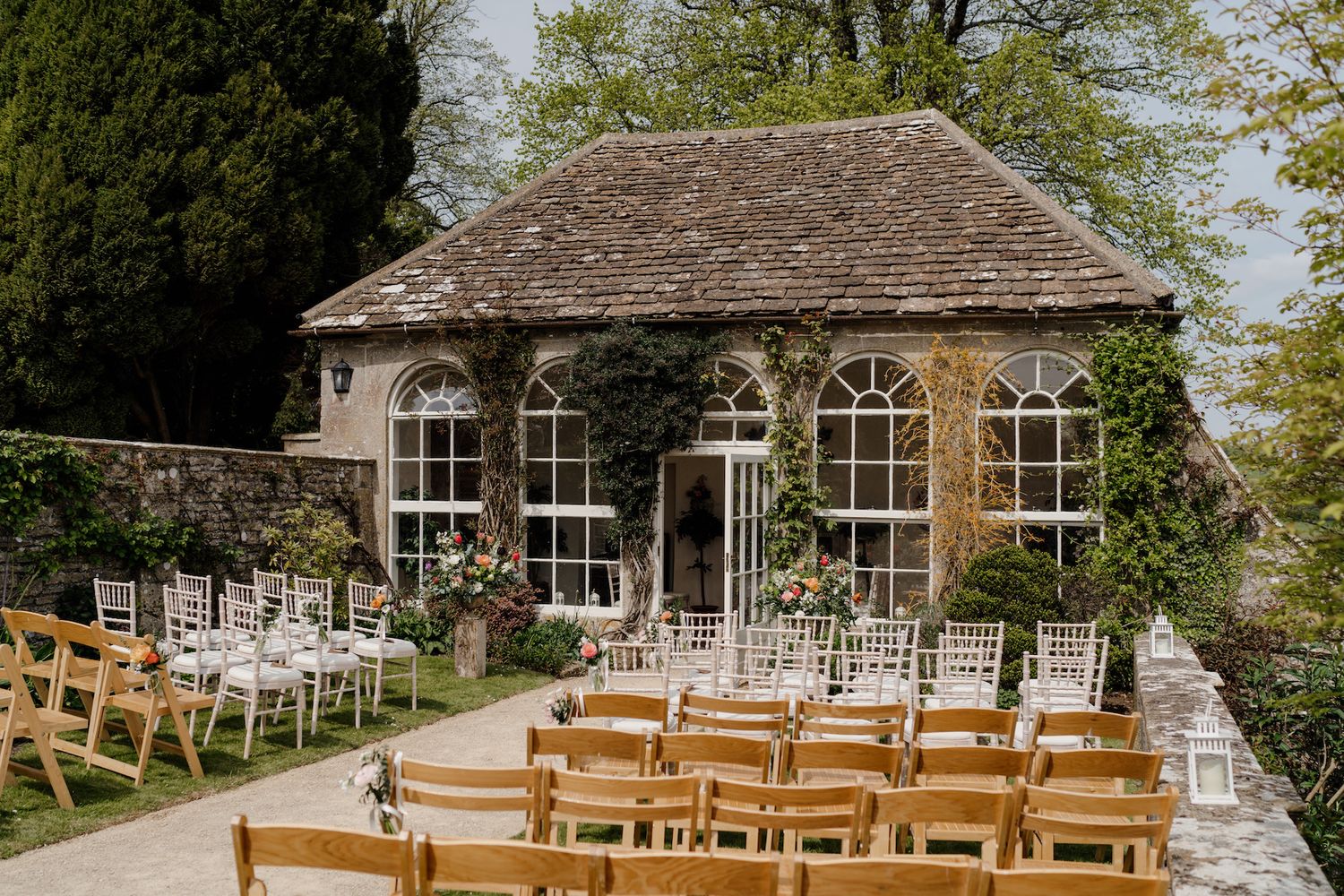 Outdoor wedding ceremony setup with wooden chairs arranged in rows beneath leafy trees.
