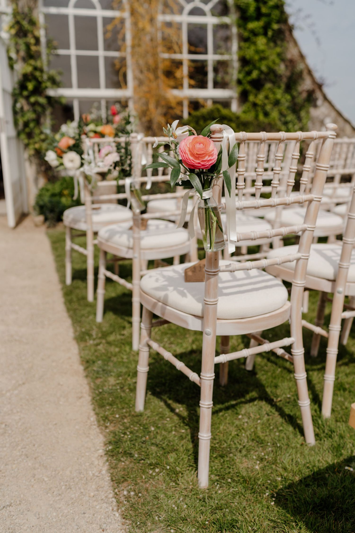 Rustic white wooden chairs lined up for an outdoor garden wedding ceremony.