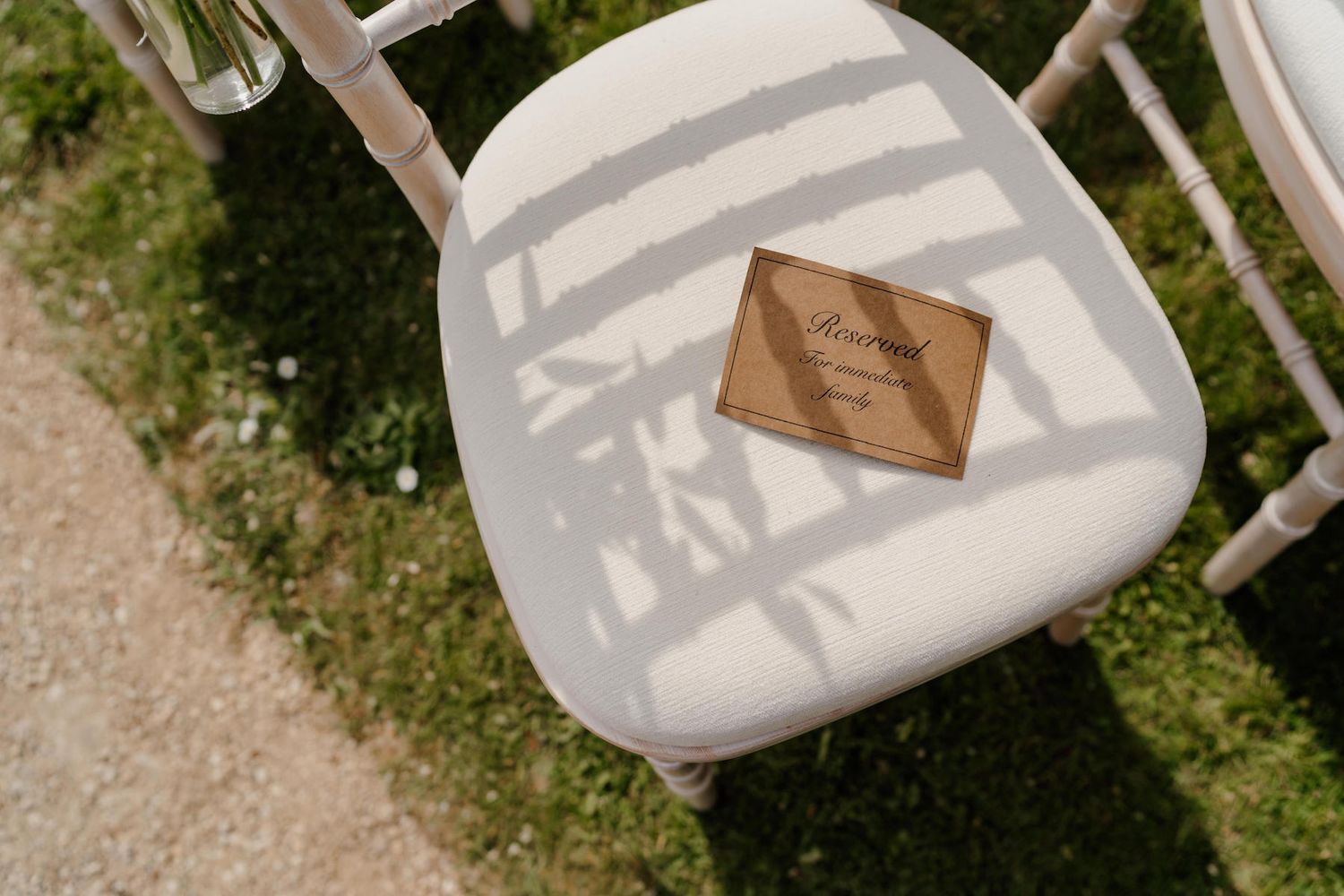White outdoor ceremony chairs positioned with floral arrangements on a sunny day.