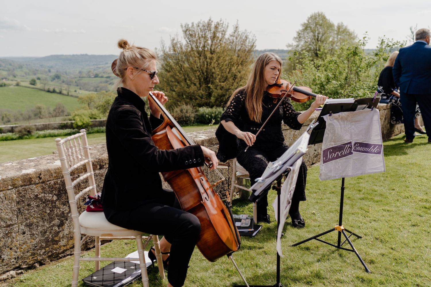 String quartet performs live music outdoors on a grassy hillside during a wedding.