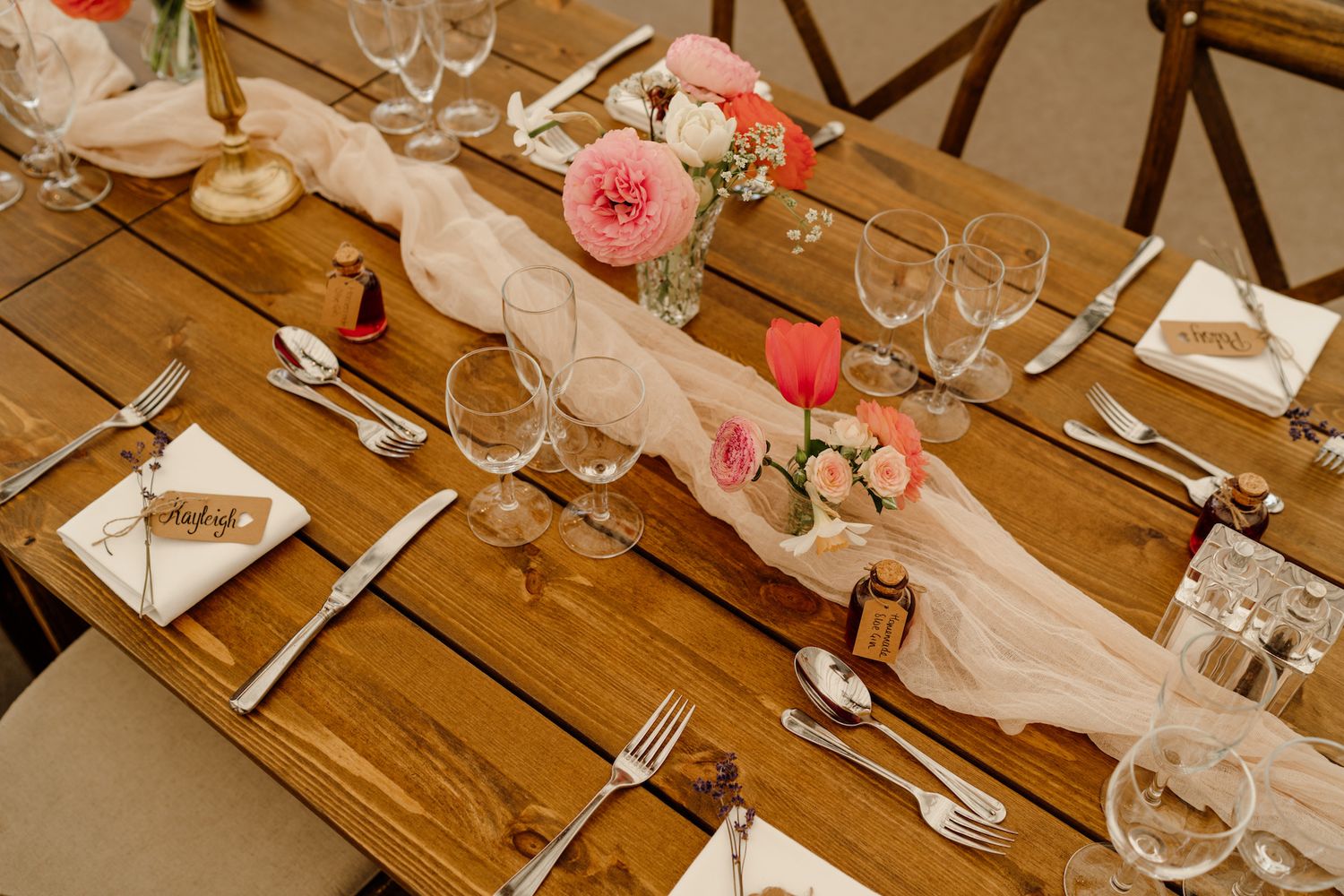 Long wooden banquet tables set with elegant glassware and pink floral arrangements for a wedding reception.
