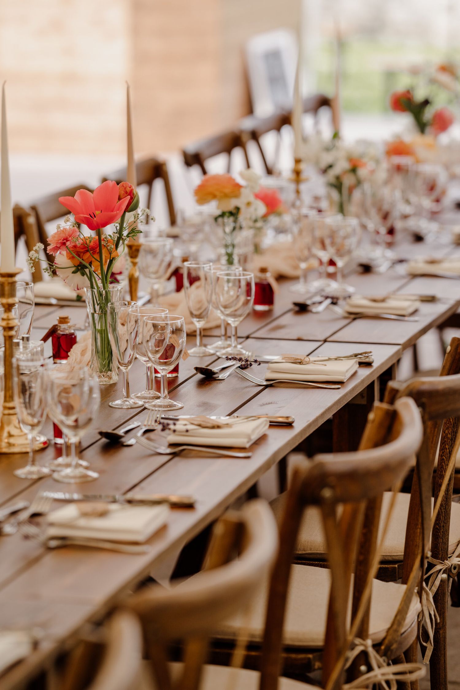 Close-up of elegant table settings with pink flowers and wine glasses on wooden farmhouse tables.