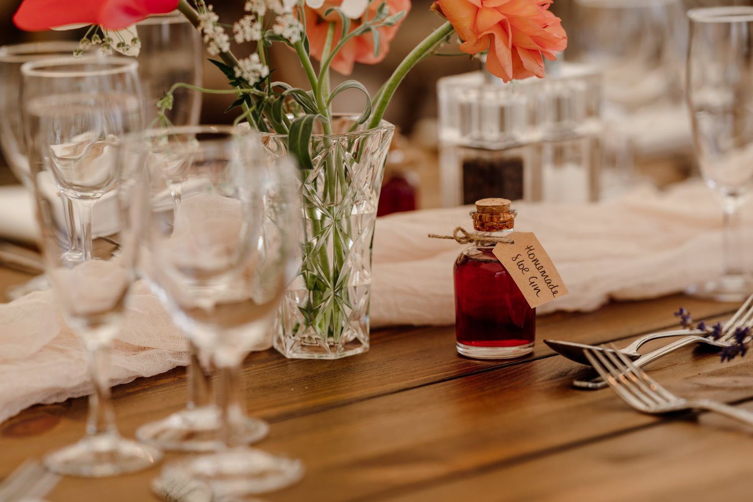 Coral-colored flowers in glass vases decorate rustic wooden dining tables with formal place settings.