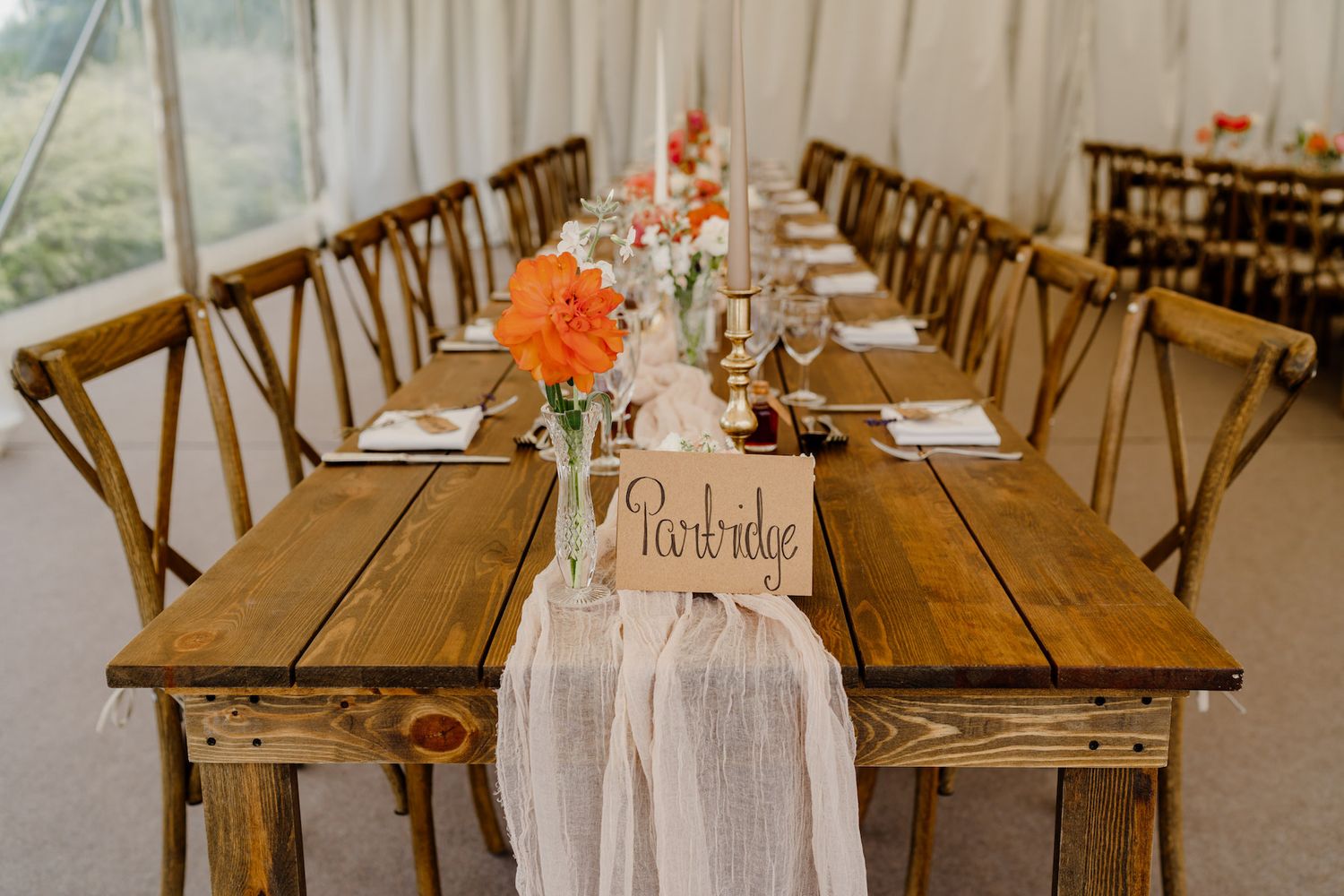 White tent reception venue featuring long wooden tables with greenery and classic table settings.