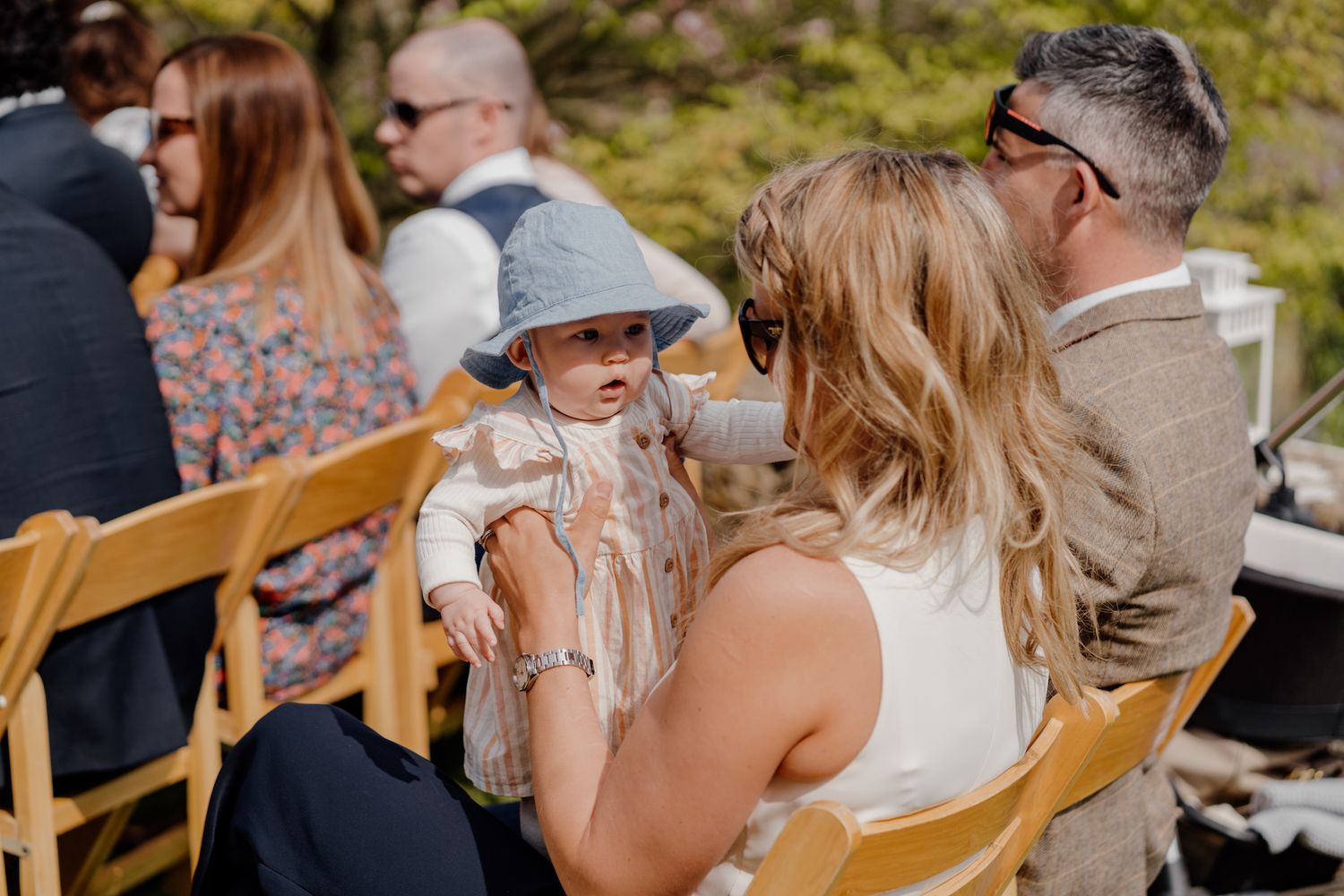 Wedding guests seated at outdoor reception chairs engaged in conversation.