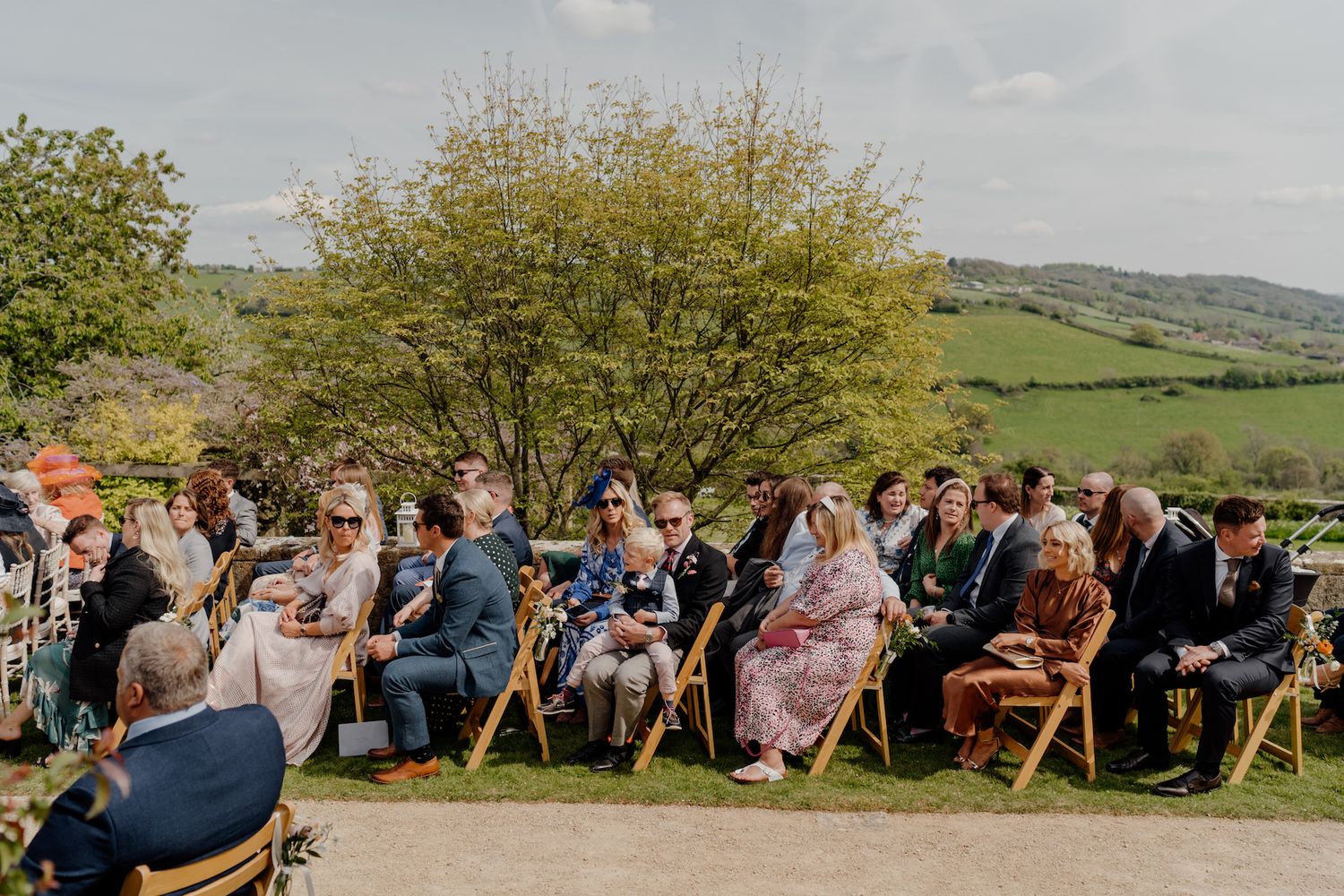 Wedding guests seated on wooden chairs during an outdoor hillside ceremony.