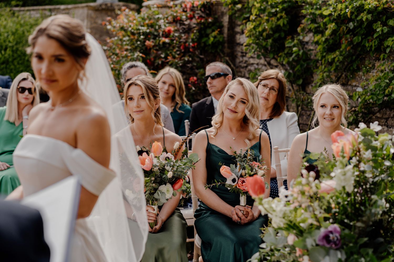 Wedding party gathered outdoors with bridesmaids in dark green dresses.