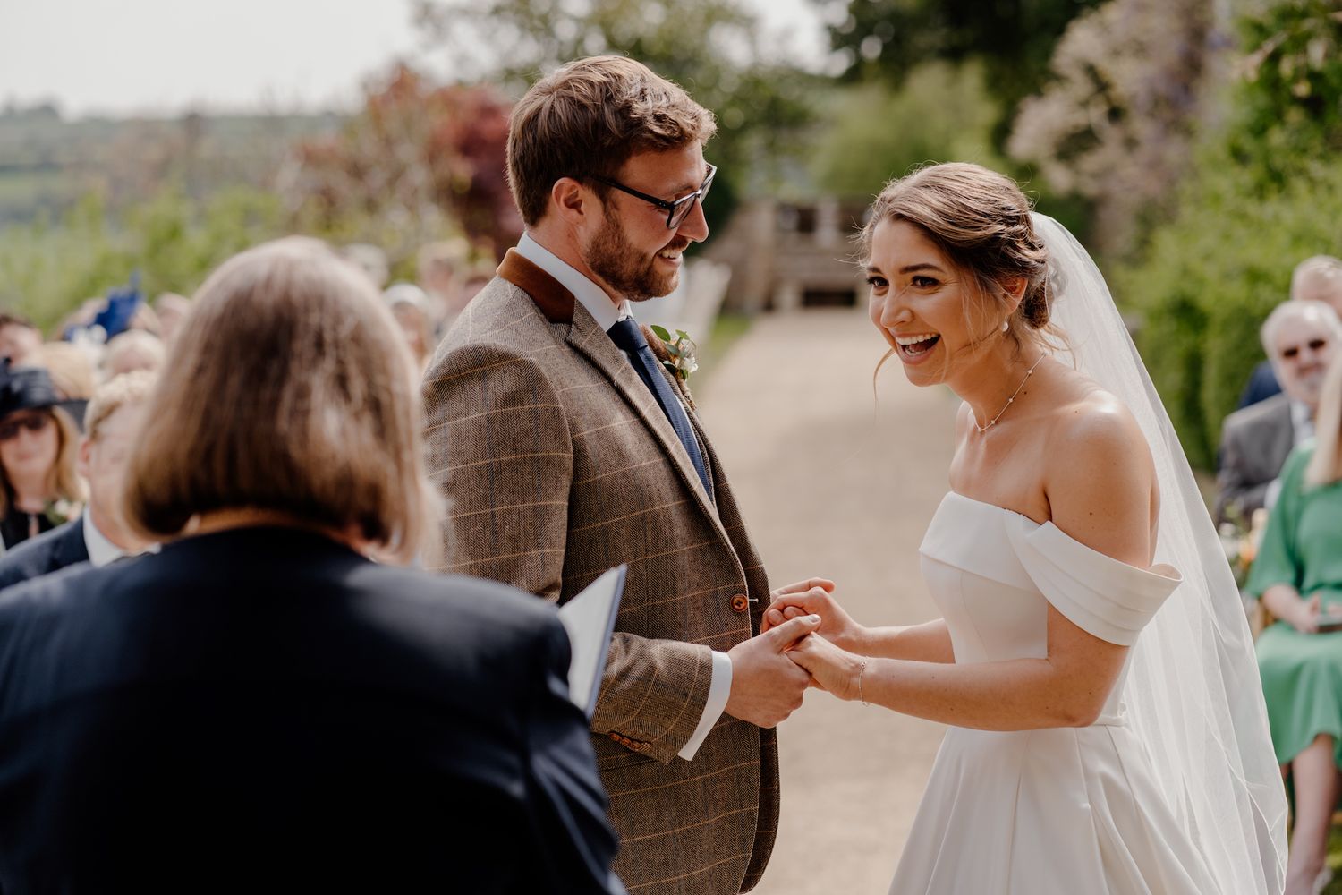 Outdoor wedding ceremony with guests watching couple exchange vows in natural lighting.