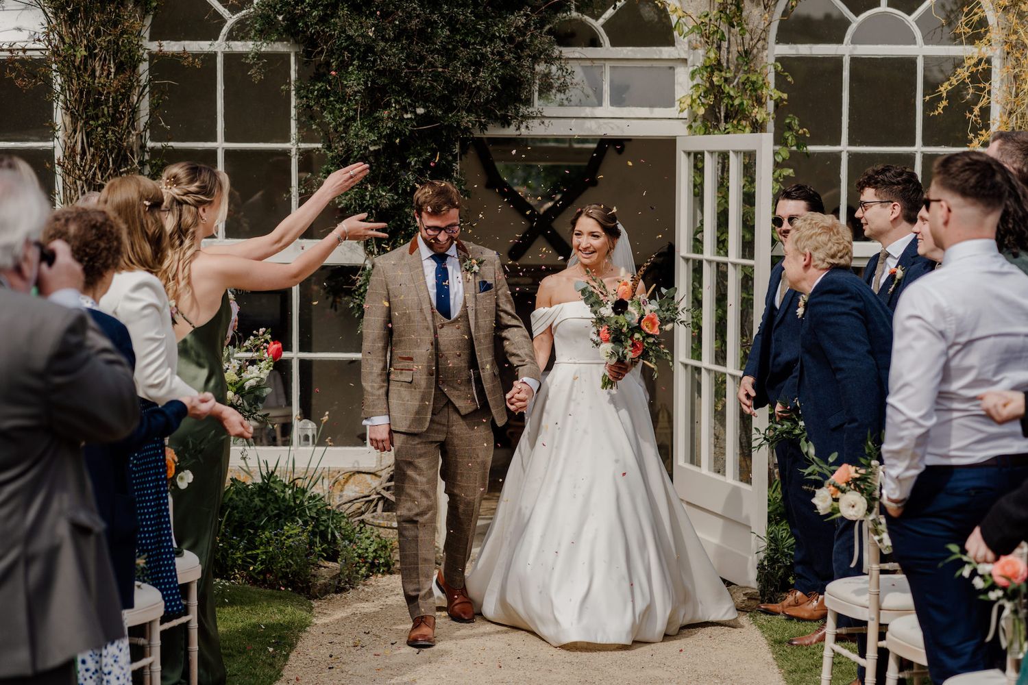 Wedding party celebrating on a stone patio with guests throwing confetti.