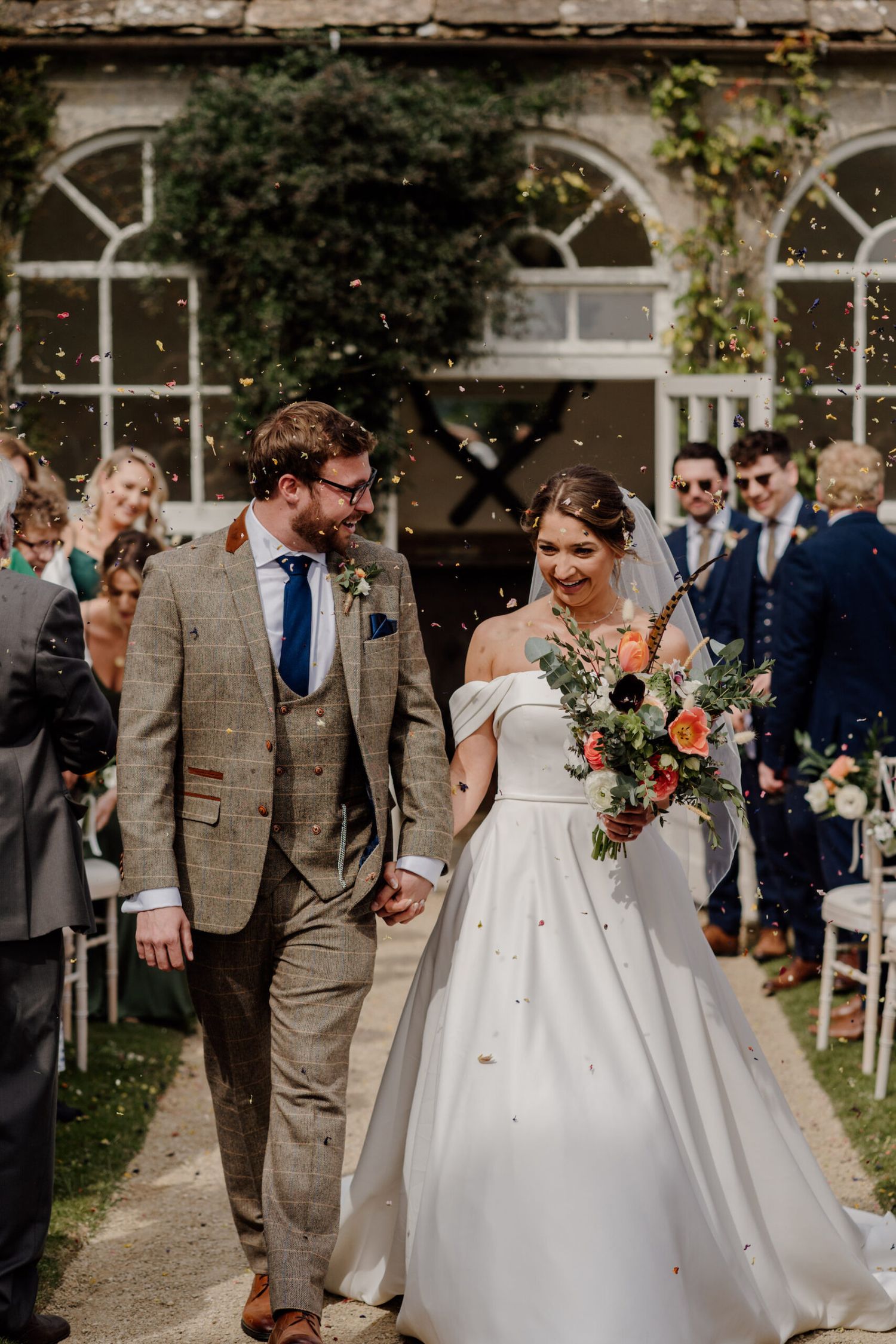 Wedding celebration with bridal party walking outdoors near rustic stone architecture.