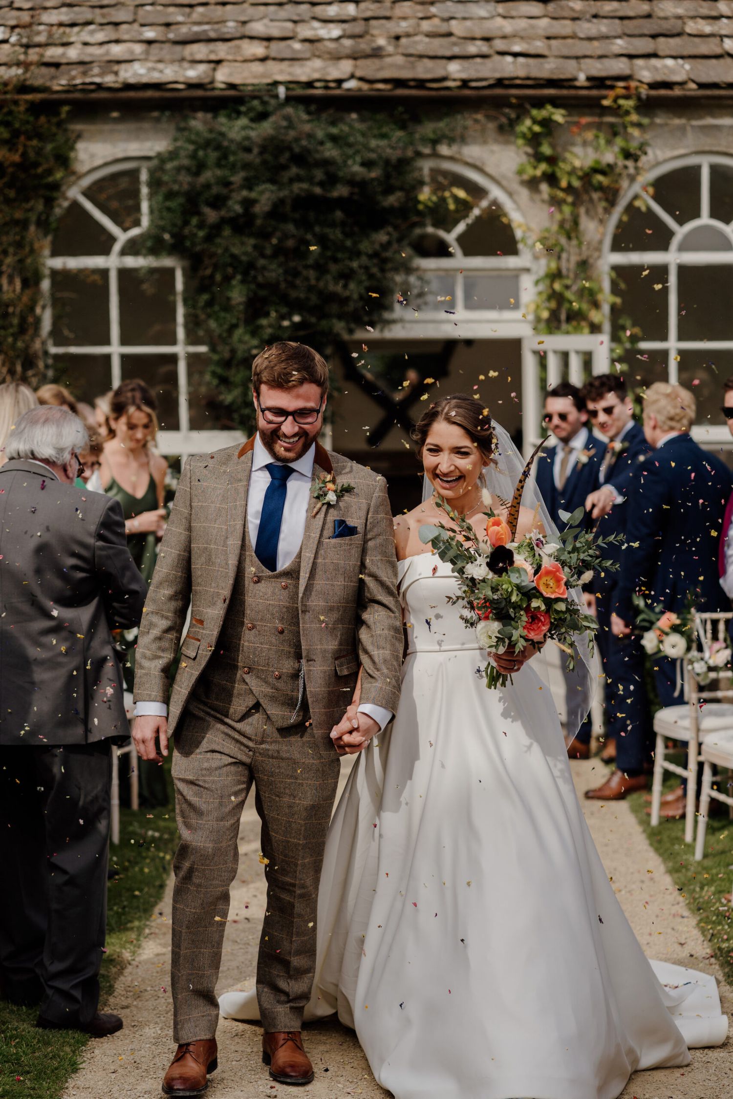 Joyful wedding recessional with confetti being thrown as couple walks down garden path.