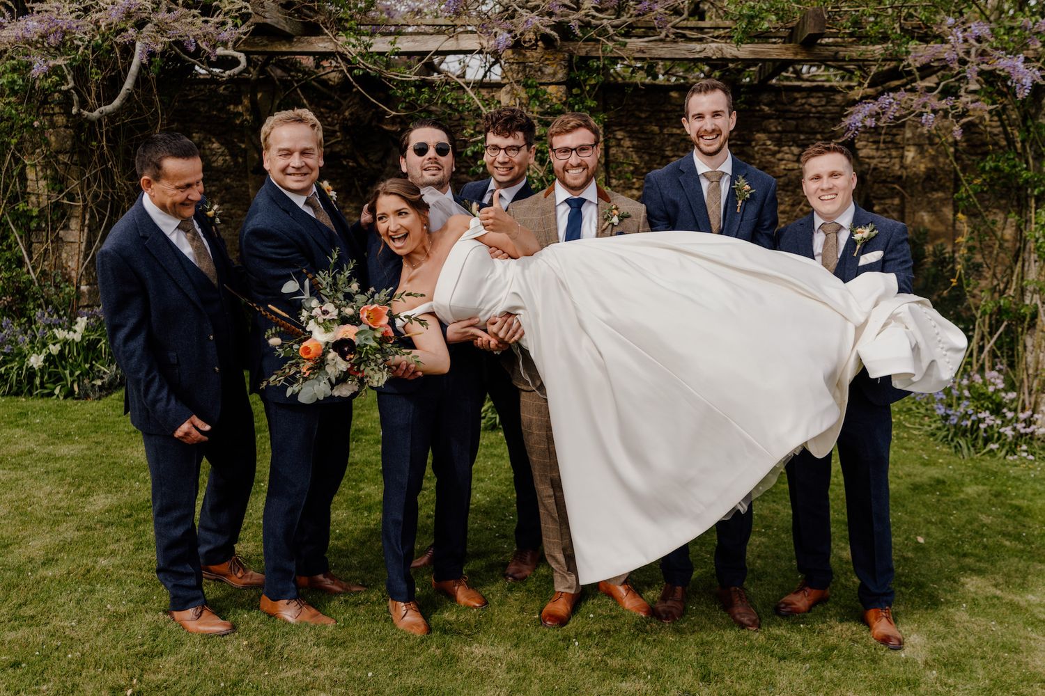 Wedding party posing on grass with bridesmaids in emerald dresses.