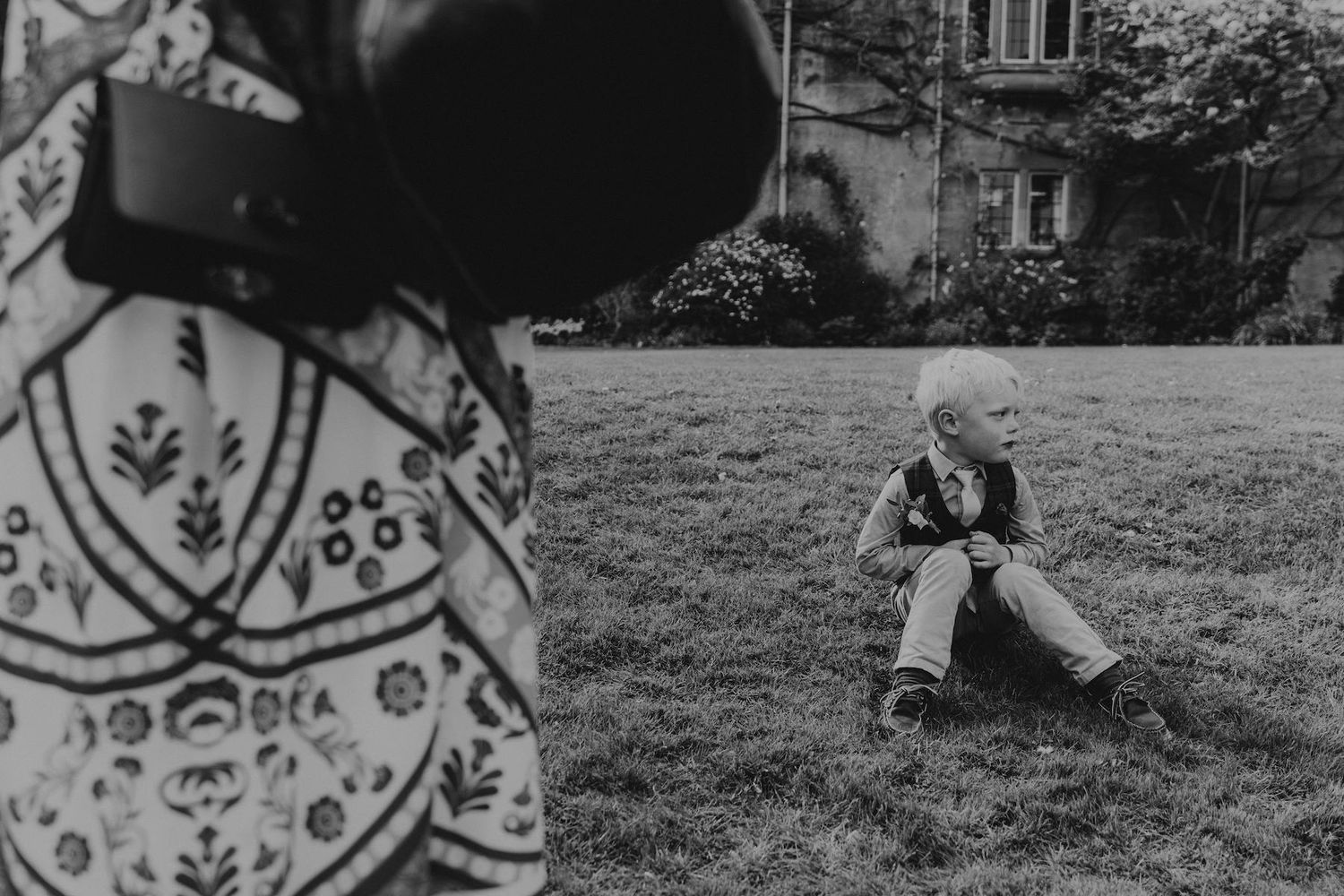 Black and white photo of photographer capturing candid moments at outdoor wedding.