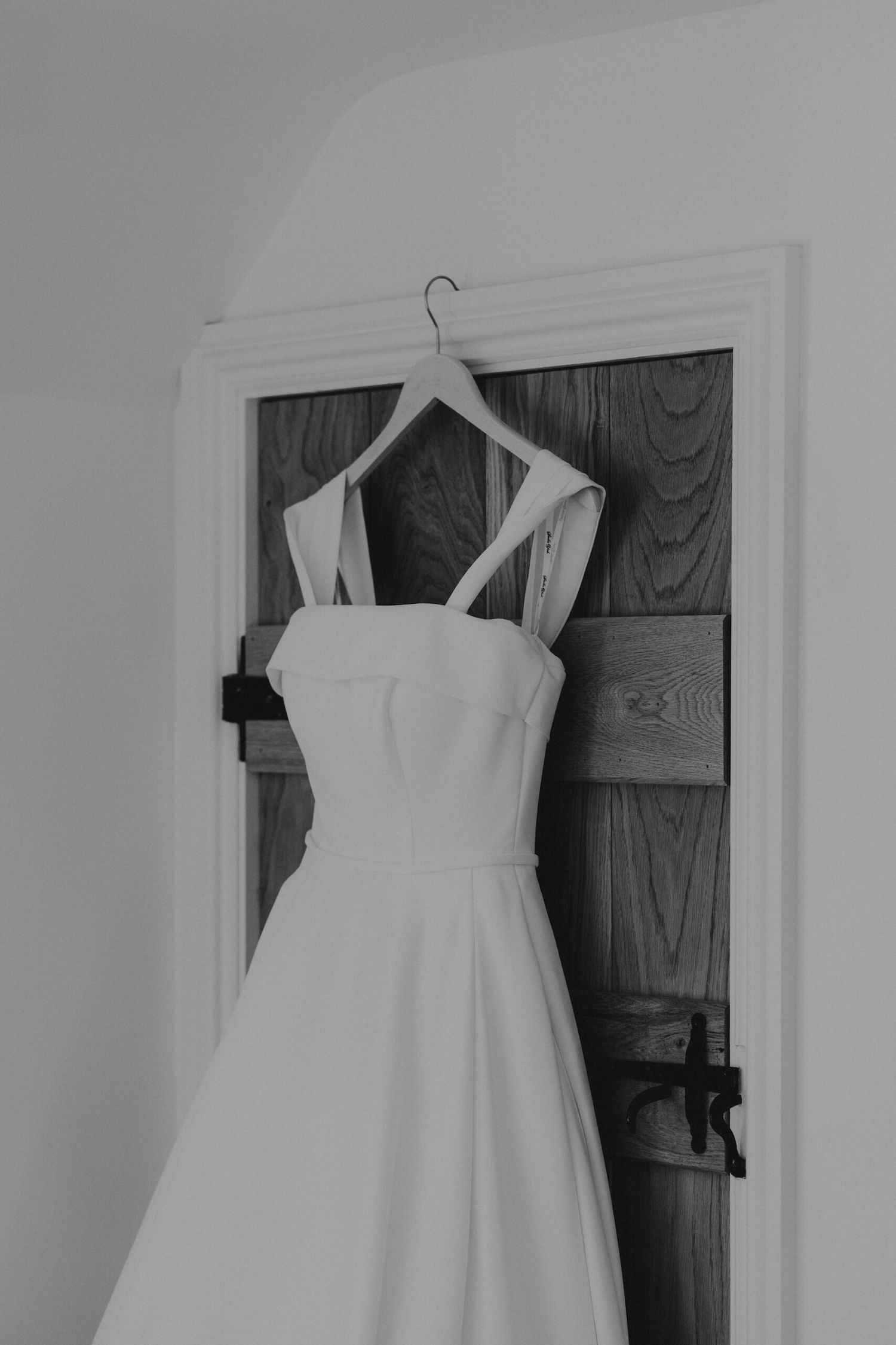 White wedding dress hanging on a wooden door against a light colored wall.