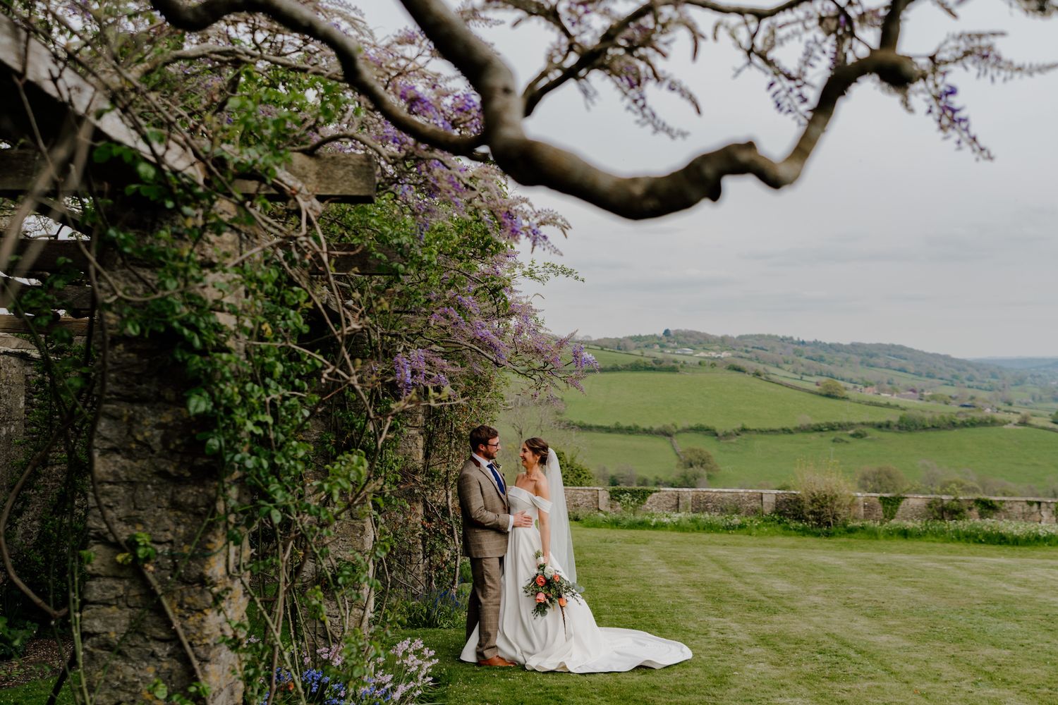 Spring blossoms frame a scenic countryside wedding venue with rolling hills in the background.