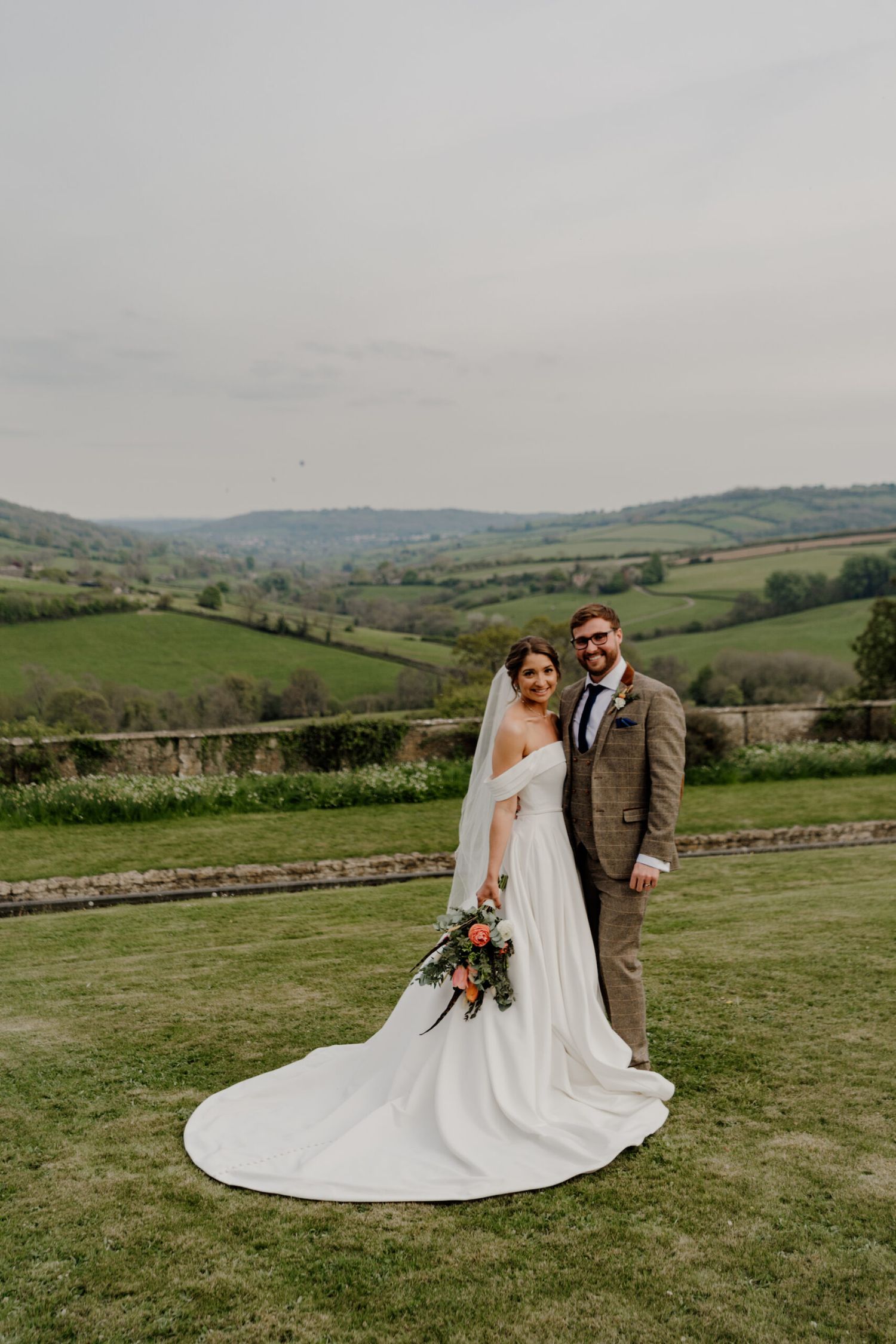 Newlyweds share a romantic moment on a hilltop overlooking rolling green countryside.