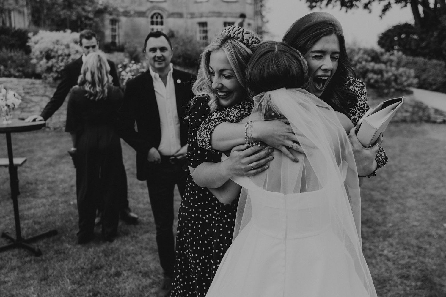 Wedding guests share emotional embraces during an outdoor garden celebration.