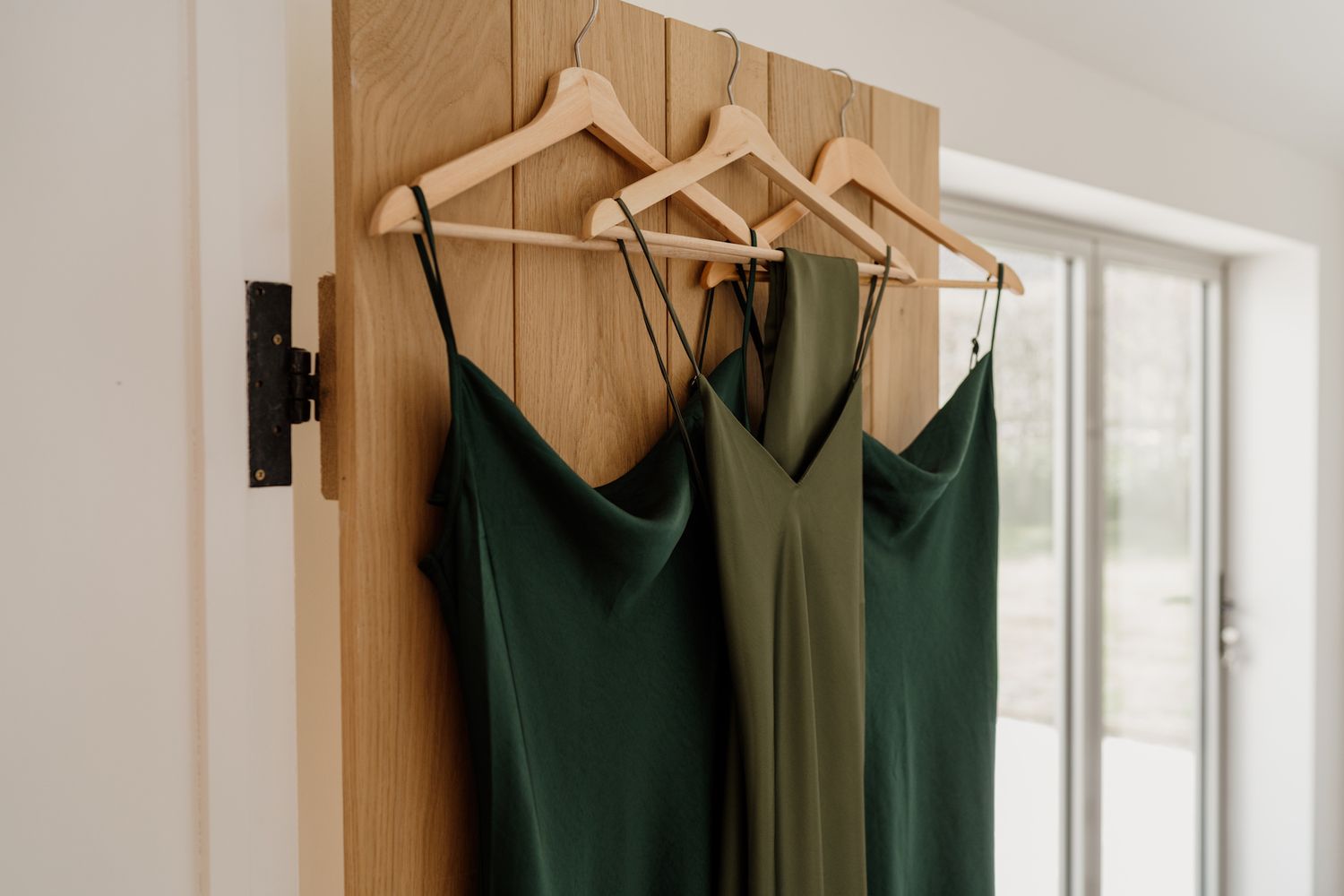 Green bridesmaid dresses hanging on wooden hangers against a white wall.