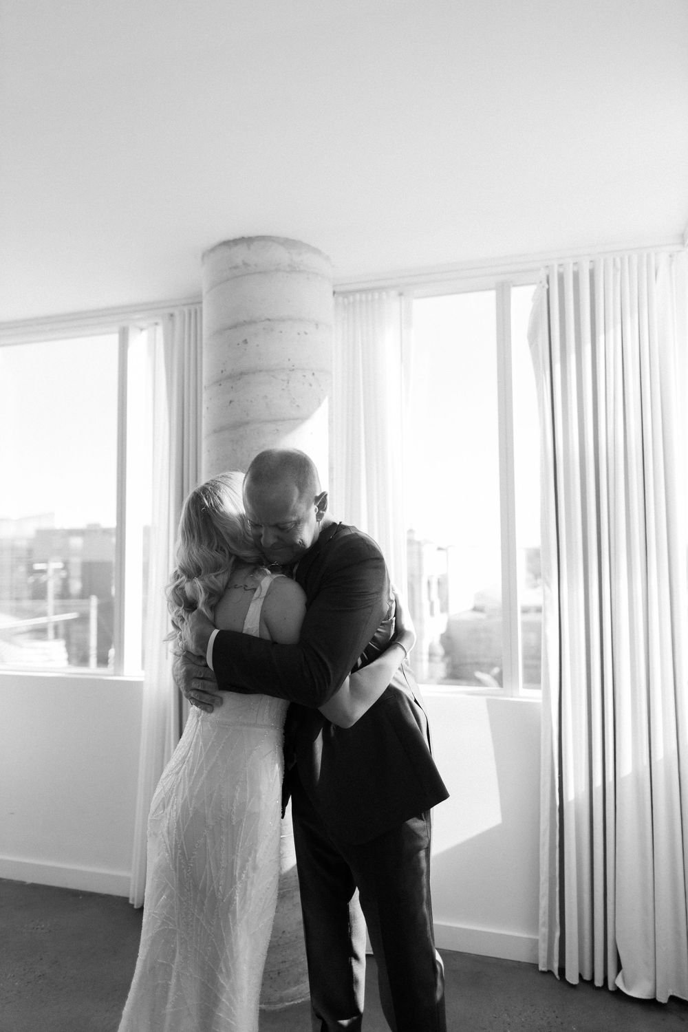 Black and white intimate moment of couple embracing in bright modern room with city views.