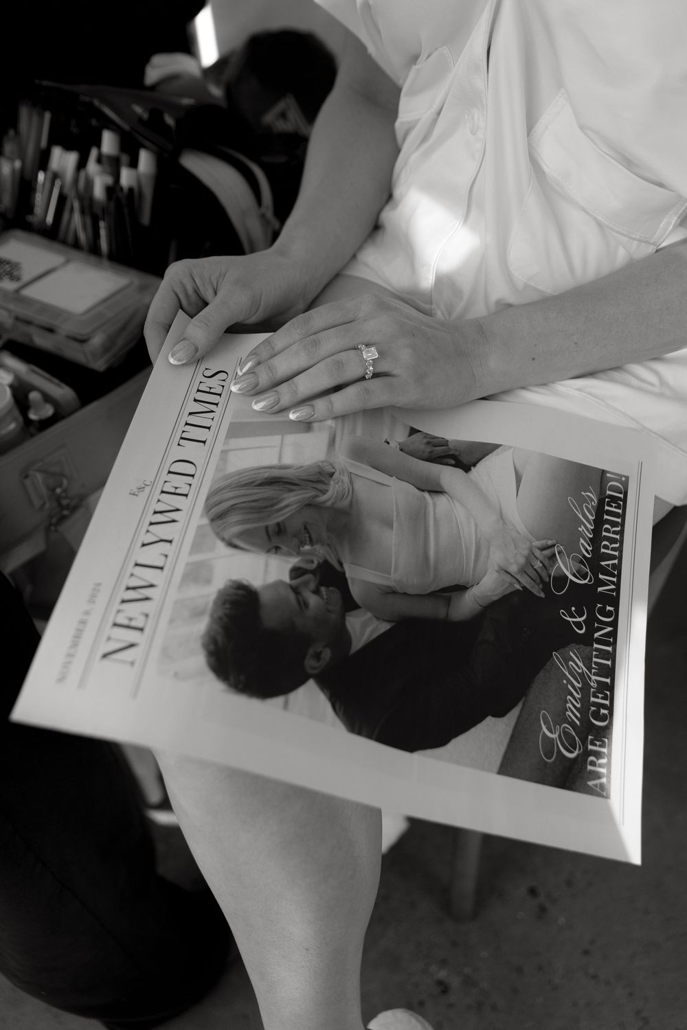 A close-up black and white photo of hands holding a wedding album or photo book with a ring visible.