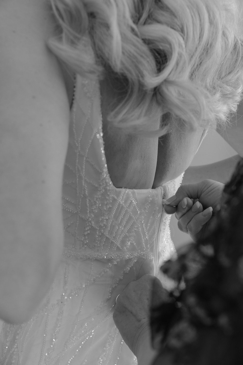 Close-up black and white photo showing the intricate beading detail on a wedding dress being fastened.