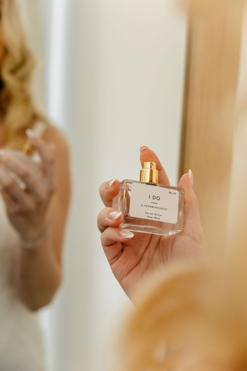 Hand holding an elegant perfume bottle with gold accents against a blurred mirror reflection.