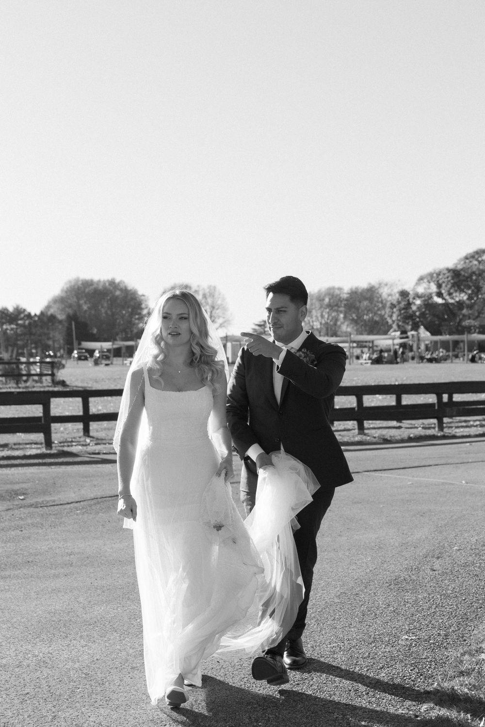 Wedding couple walking playfully through an outdoor venue with wooden fences in black and white.