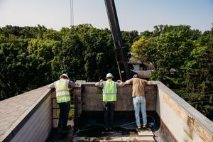 Workers installing waterproof membrane on a flat commercial rooftop during a bright sunny day.