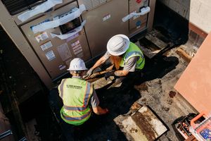 Construction workers in safety gear install heavy equipment through warehouse loading dock access point.