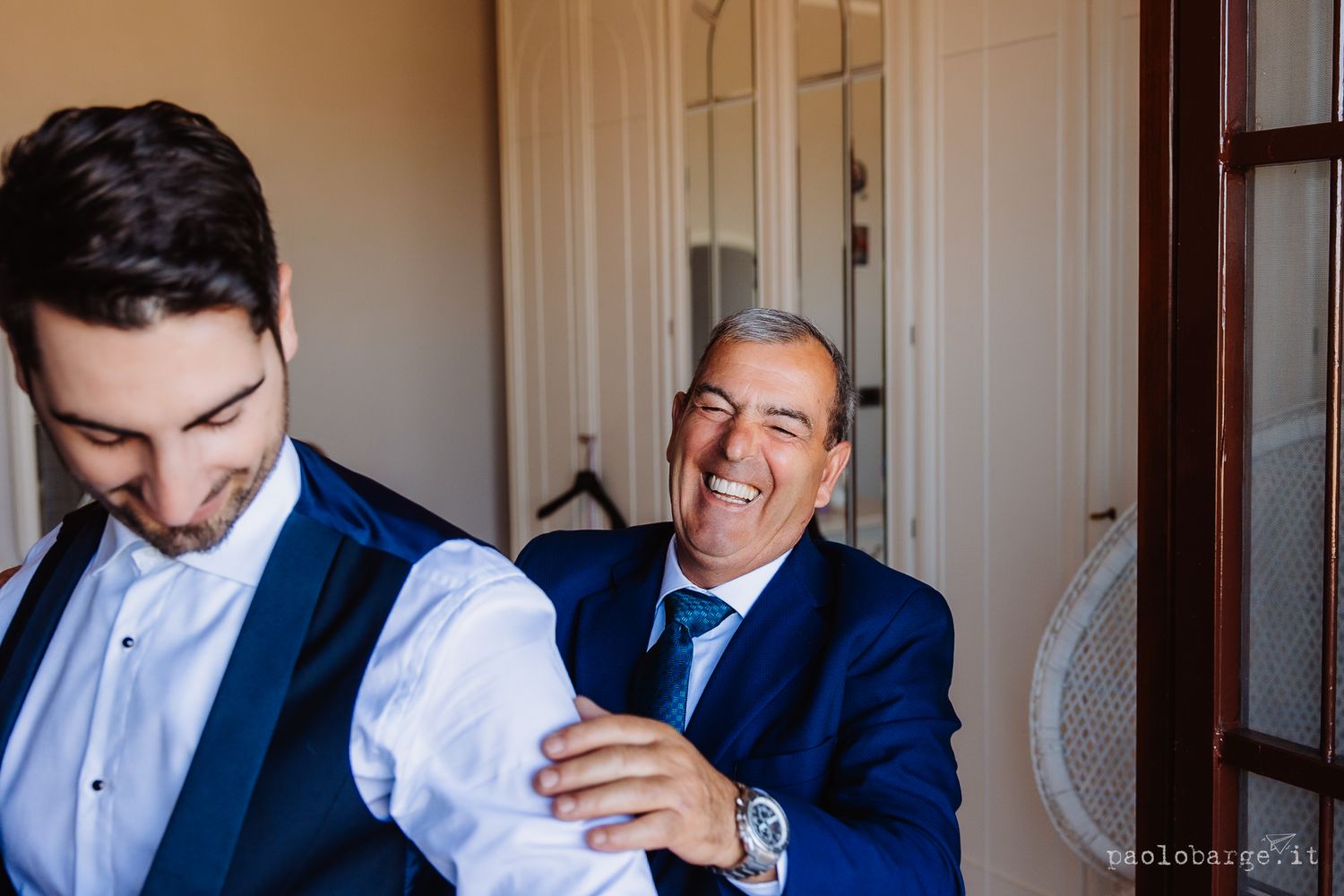 Groomsmen in navy blue suits help each other prepare and adjust their formal attire before a wedding ceremony.