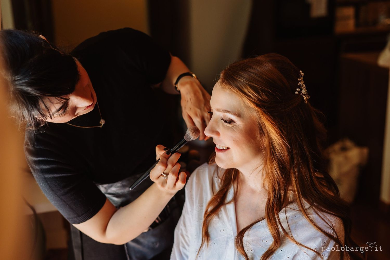 Professional makeup artist applying eyeshadow to client in soft lighting for wedding preparation.
