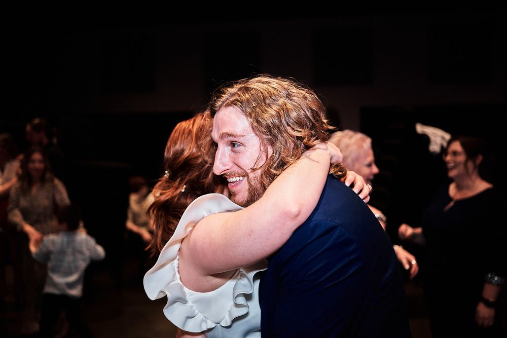 Couple embraces while dancing among other people on a dark dance floor during a social gathering.