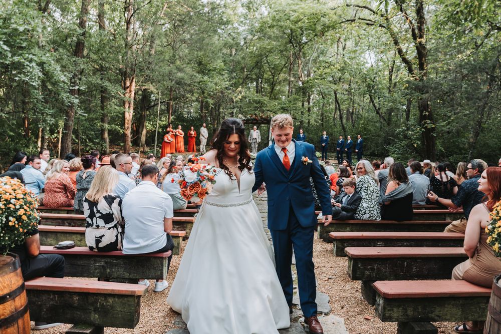 Wedding ceremony in a forest setting with wooden benches and floral decorations.