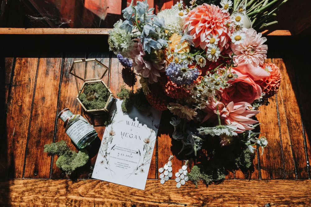 Wedding details featuring a floral arrangement with invitation card on wooden surface.