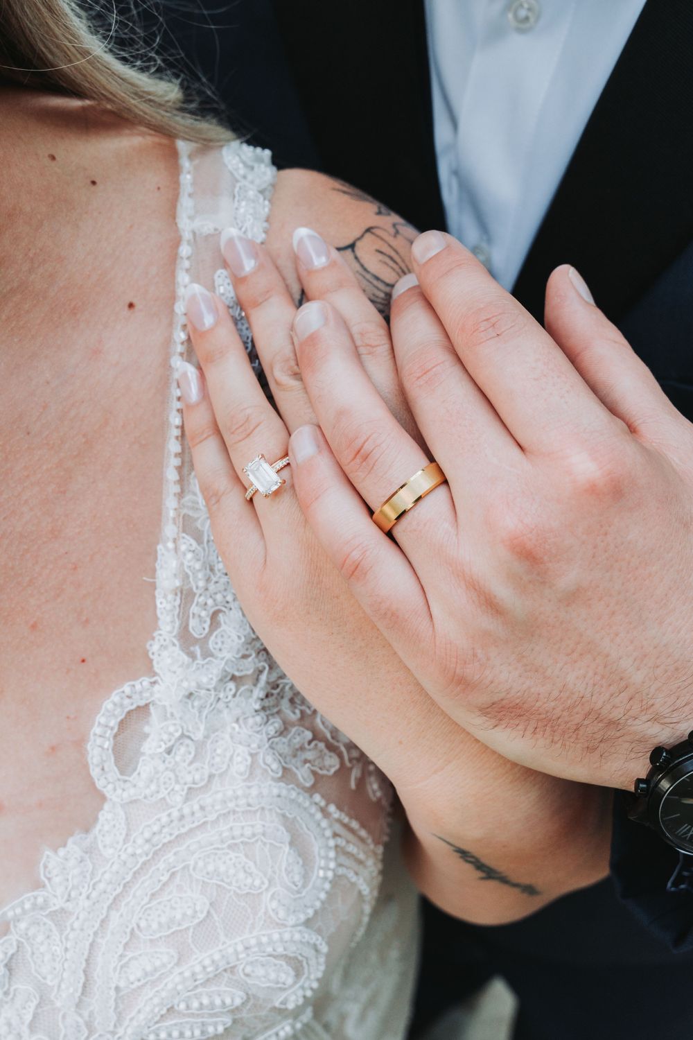 Close-up of newlywed couple's hands showing wedding rings and lace dress detail.