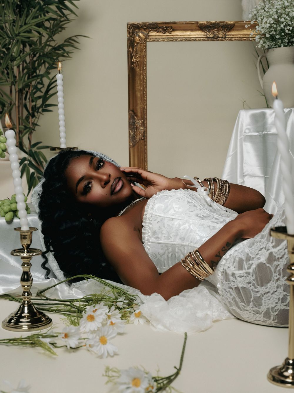 Artistic portrait series of someone laying on a white table with candles and floral decorations in an ethereal setting.