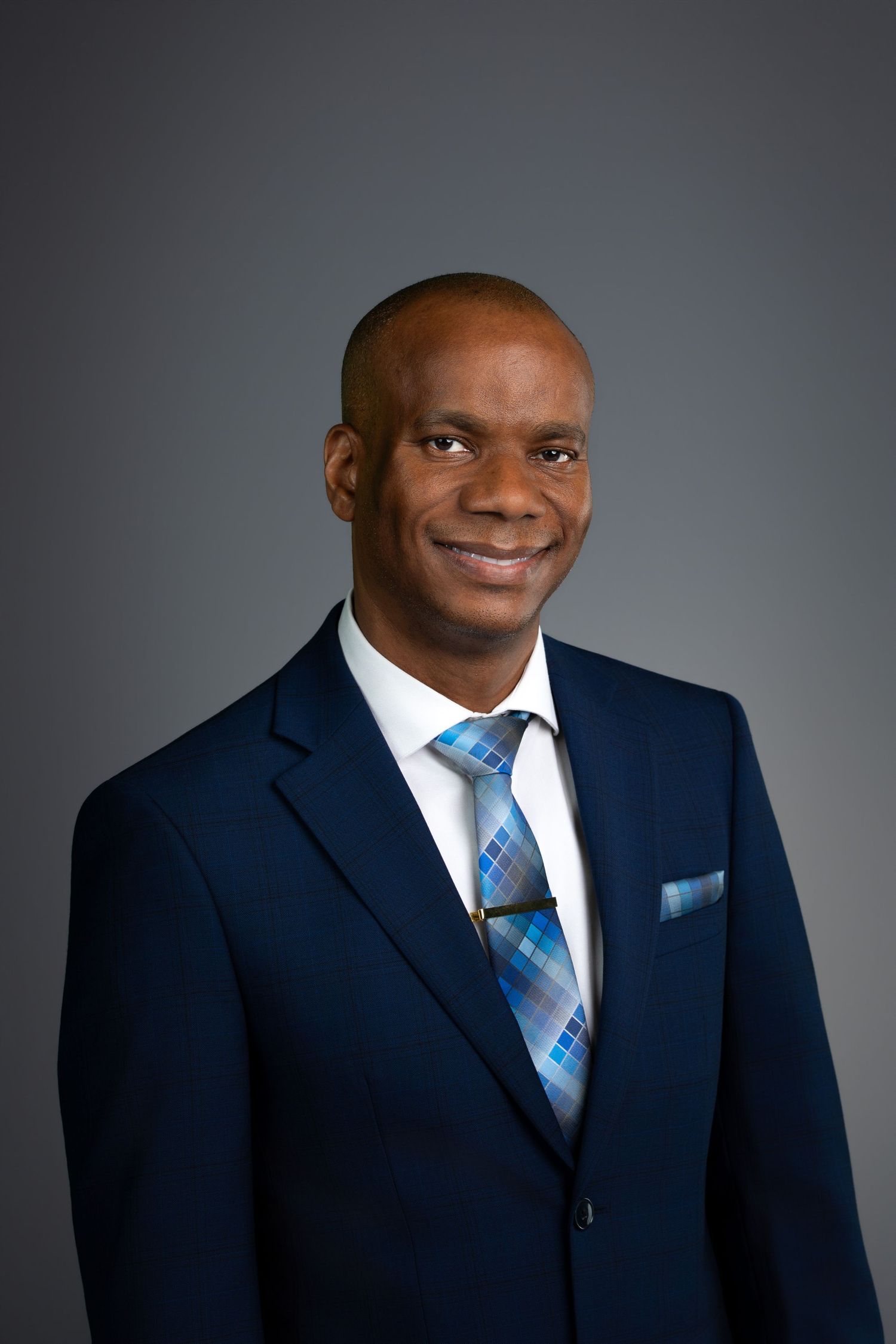 Professional headshot portrait of person in white shirt against brown backdrop.