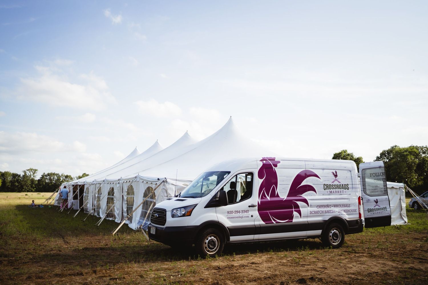 A row of white event tents and service vehicles lined up on a grassy field for an outdoor gathering.