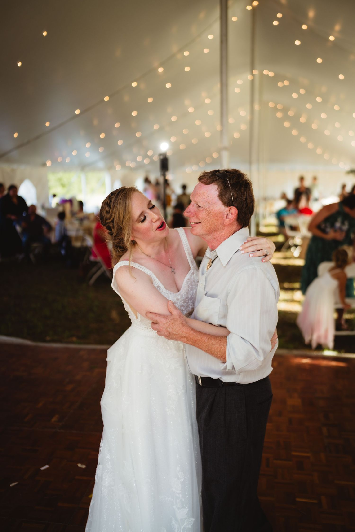 Wedding couple shares a sweet dance moment under twinkling lights in a reception tent.