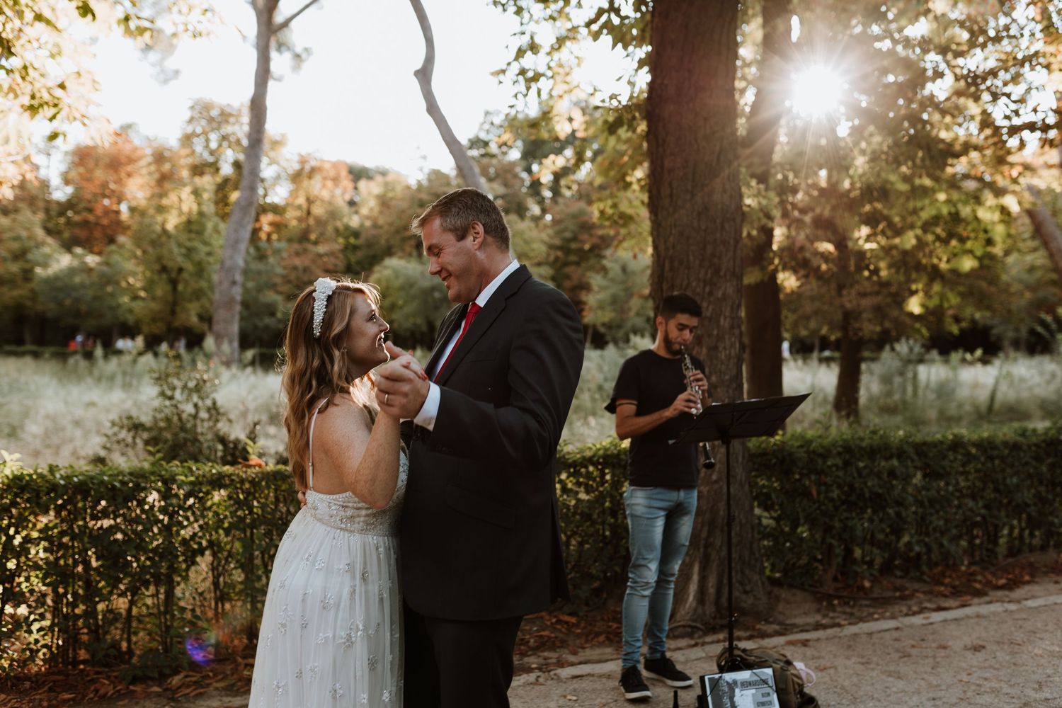 Romantic couple dancing at sunset in a garden while musician performs in the background.