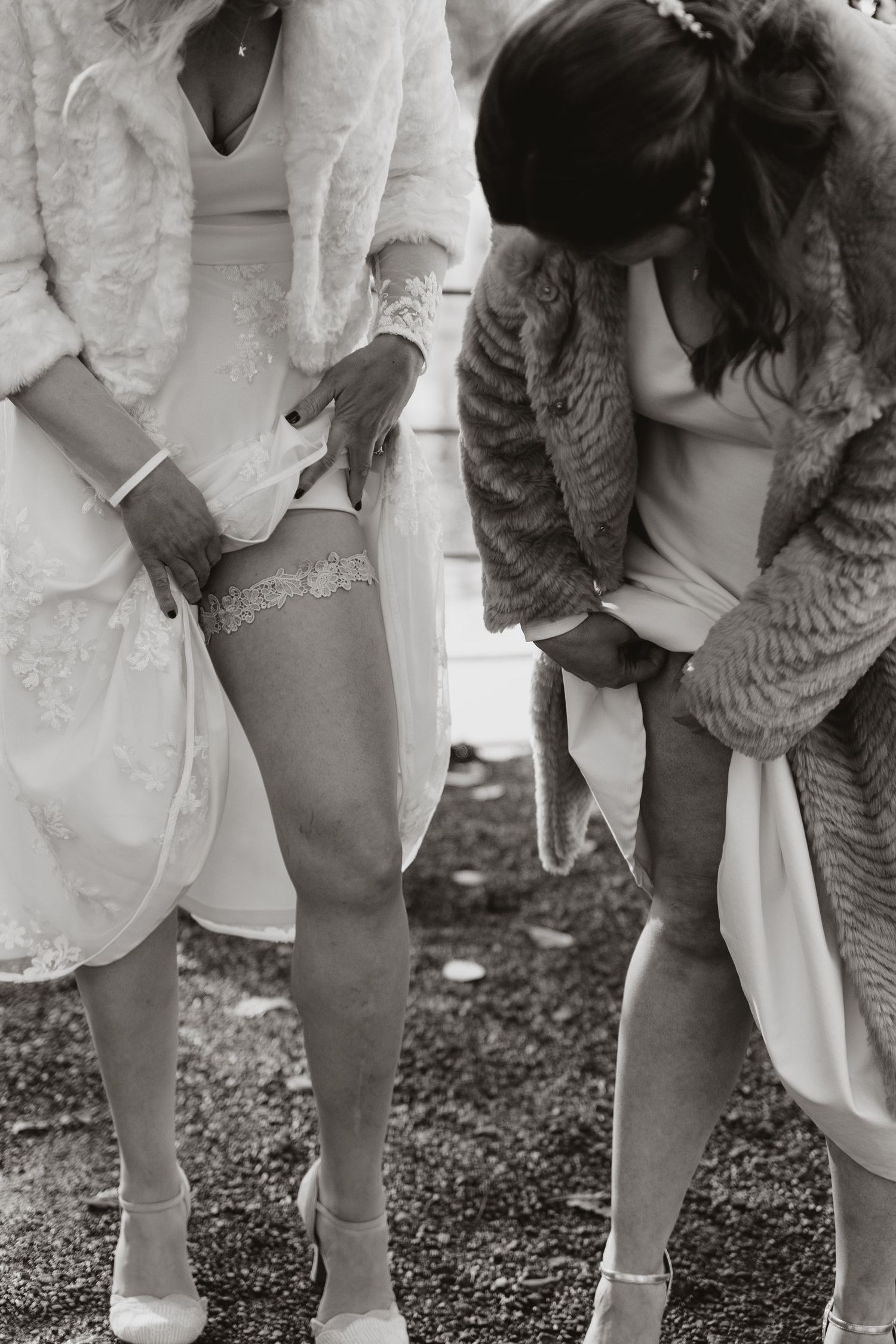 Black and white photo showing detailed lace garters and white heels on legs with elegant fur coats and dresses.