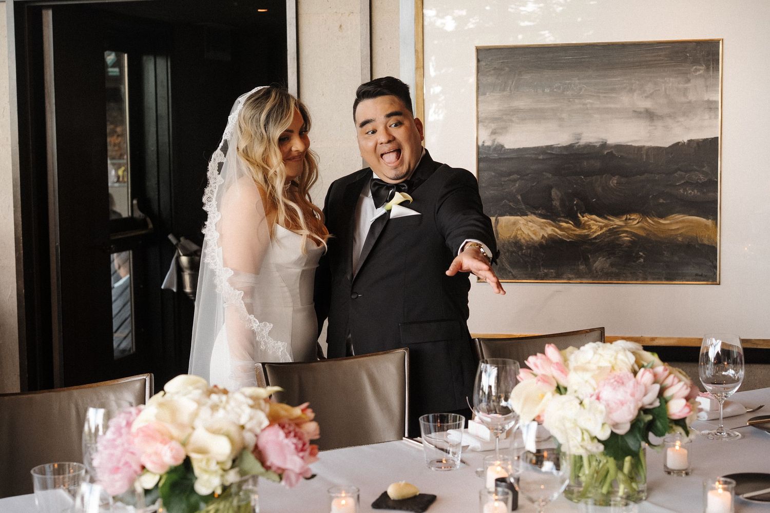 A couple celebrates joyfully together at their wedding reception beside elegant floral centerpieces and table settings.