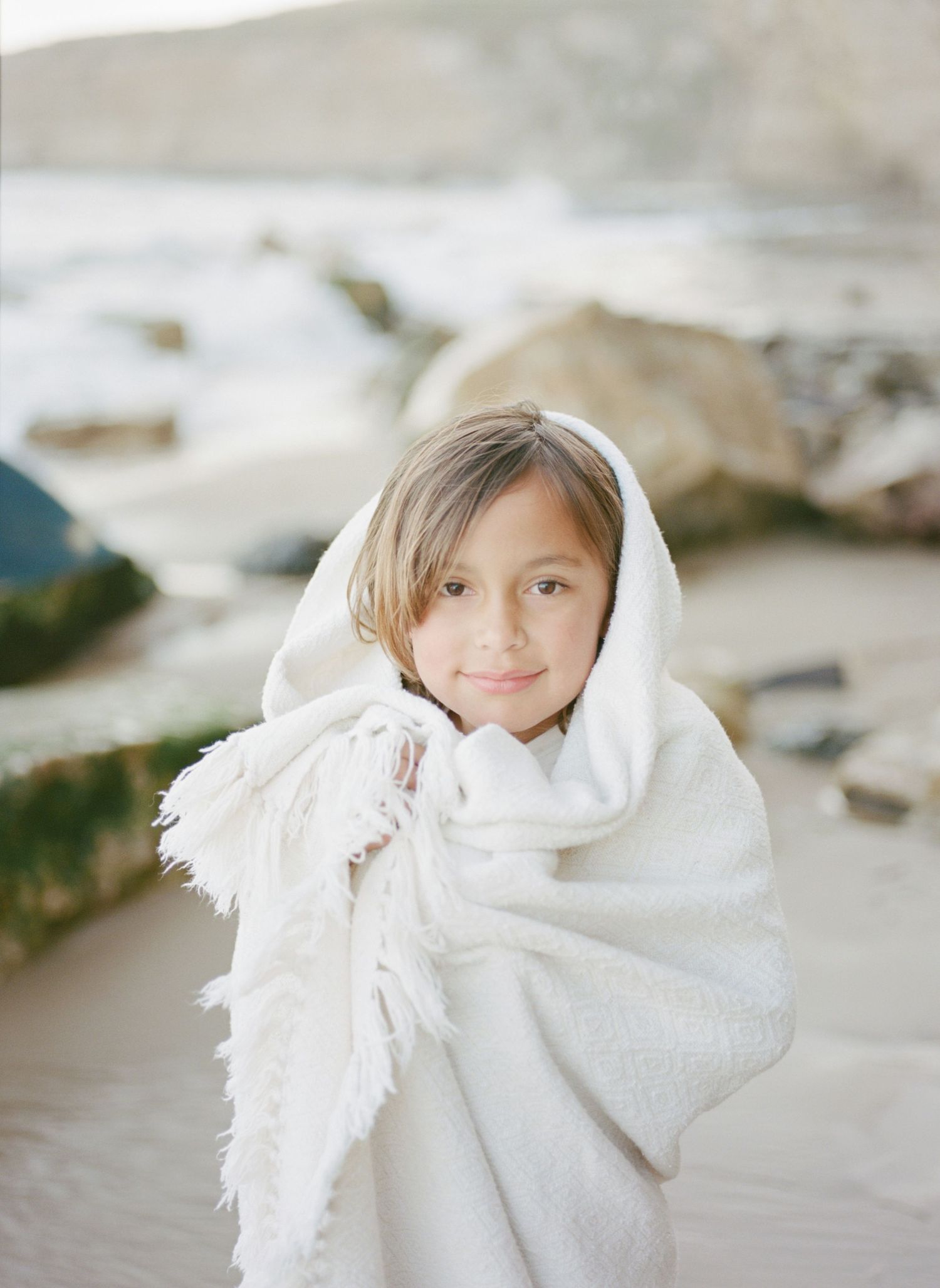 Ethereal and dreamy portrait series showing figure wrapped in soft white fabric at a beach setting in muted tones film by Chelsee Rawe .
