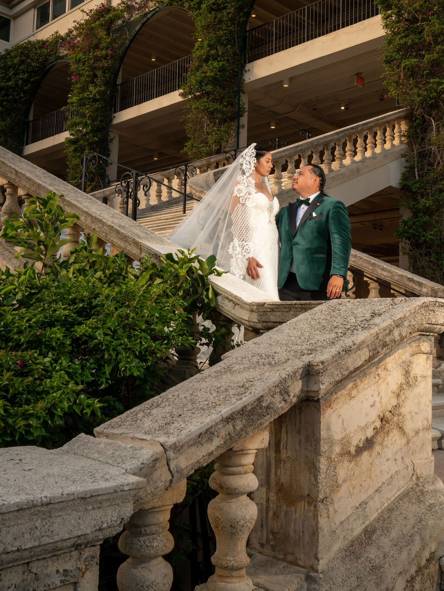 Elegant wedding couple poses on grand stone staircase with greenery in a series of romantic shots.