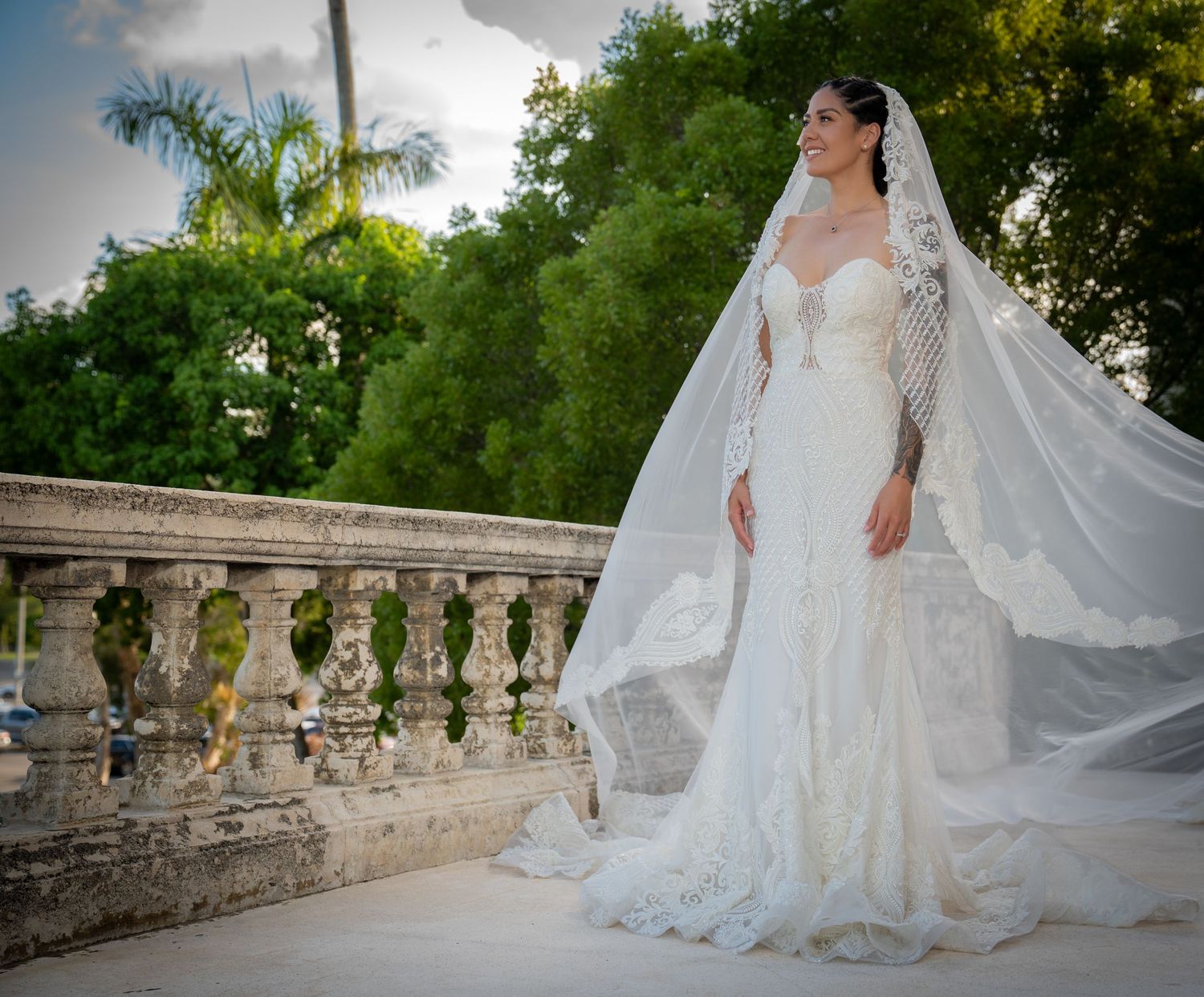A flowing white lace wedding dress with a long train photographed across multiple angles on a stone balcony.