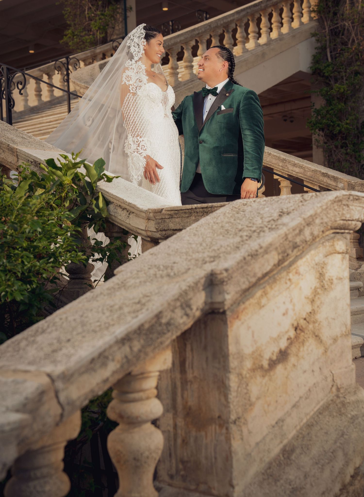 Wedding couple poses together in front of elegant stone balustrade at dusk in romantic outdoor setting.